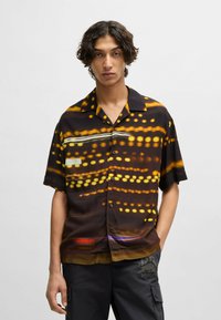 Short-sleeve shirt in black with abstract yellow and orange light patterns, featuring a notched collar and button closures.
