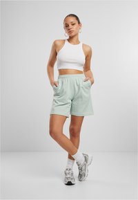 Light green shorts with an elastic waistband and side pockets, paired with a white sleeveless crop top and gray athletic shoes.