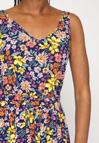 Květinové šaty s v-výstřihem, živým námořnickým pozadím a kombinací růžových, žlutých a oranžových květin se zúžením v pásu.