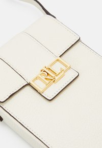 Vit läder crossbody-väska med en texturerad yta, prydd med ett spänne i guldton och en mörk kantdetalj. Kompakt och rektangulär design.