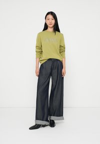 Ελιόχρωμο φούτερ με υφή στο μπροστινό μέρος, συνδυασμένο με φαρδιά τζιν παντελόνια από σκούρο denim με γυρισμένα μπατζάκια και μαύρες μπότες.