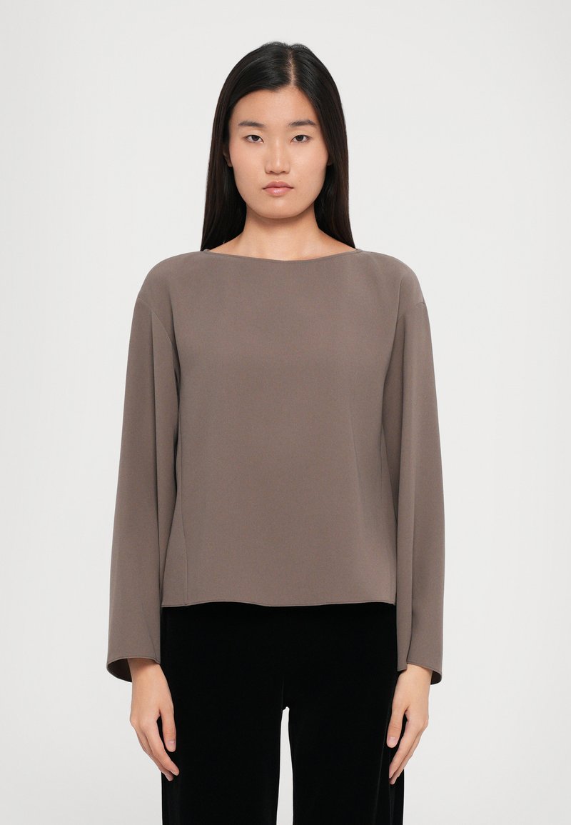 Brown long-sleeve top with a boat neckline, featuring a smooth texture and relaxed fit, paired with black trousers. Minimalistic design.