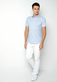 Hellblauses Kurzarm-Hemd mit Knöpfen, slim fit, aus weichem Stoff. Kombiniert mit weißen, slim-fit Hosen und weißen Sneakern.