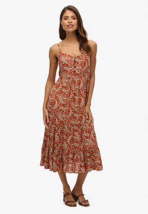 Maxi jurk in roestbruin met witte paisleyprint. Spaghetti bandjes, knoopdetails aan de voorkant en een uitlopende zoom. Lichtgewicht stof.
