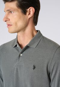 Polo grigio realizzato in morbido tessuto, con colletto classico, patta con tre bottoni e un piccolo logo nero sul petto.
