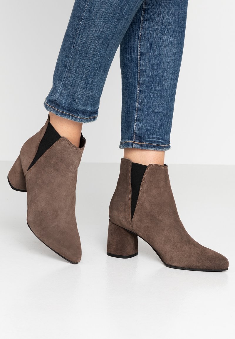 Bottines en daim marron avec un bout pointu, des panneaux latéraux élastiques et un talon carré, associées à un jean bleu cropped.