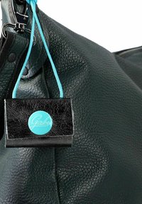 Borsa in pelle nera testurizzata con una tonalità verdognola. Presenta un'etichetta turchese con un logo, fissata da un cinturino blu. Hardware metallico visibile.