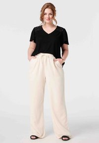 Haut noir à col en V avec des accents en dentelle sur les épaules, associé à un pantalon large crème avec une taille élastique et des poches latérales.