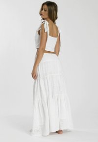 Completo bianco a due pezzi composto da un crop top con spalline annodate e una lunga gonna a strati, entrambi con ricami a occhiello e una silhouette fluida.