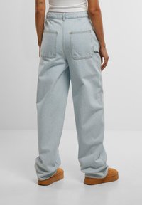 Jeans de mezclilla sueltos en azul claro, con dos bolsillos traseros y un bolsillo tipo cargo, combinados con calzado marrón de suela gruesa.