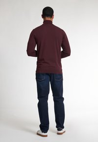 Chemise maroon à manches longues avec un col montant, associée à un jean en denim foncé et des baskets blanches avec des accents noirs. Texture lisse.
