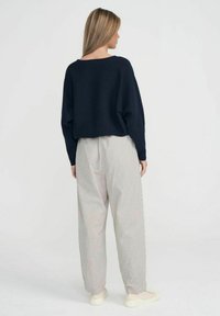 Marineblauer, beschnittenes Sweatshirt mit weiten Ärmeln, kombiniert mit hellgrauen gestreiften Hosen. Das Modell trägt beiges Sneakers.