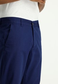 Chinos azul marino hechos de algodón, con frente plano, bolsillos laterales y cierre con botón superior. Ajuste entallado con textura suave.