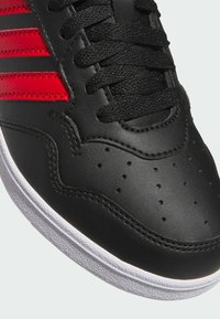 Czarne sneakersy z czerwonymi paskami, perforowanym noskiem, teksturowaną czarną skórzaną cholewką, czarnymi sznurówkami i białą gumową podeszwą.