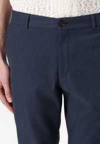 Marineblå skreddersydde bukser laget av teksturert stoff med en enkelt knappelukking og en sidelomme, med slim fit design.