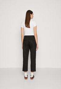 Black cropped pants with a tailored fit, featuring a waistband, pockets, and a smooth texture, paired with a white short-sleeve top and stylish shoes.