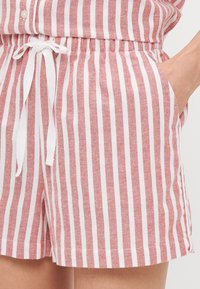 Shorts rayés rouges et blancs avec une taille élastique dotée d'un cordon de serrage, poches latérales et une finition en tissu texturé.