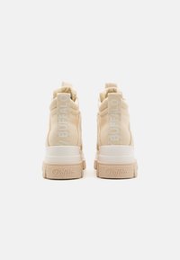 Beige høye sneakers i teksturert stoff, med hvite detaljer og en tykk såle. Har et merke på hælen og en bakre pull-tab.