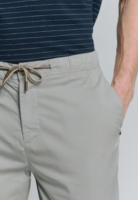 Lichtgrijze shorts gemaakt van een gladde stof met een elastische tailleband, een trekkoord met gouden hardware en zichtbare zijzakken.