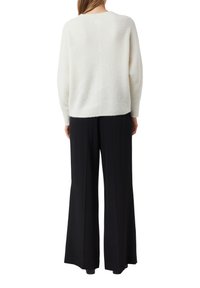 Weißer, gerippter Pullover mit lockerer Passform, kombiniert mit hoch taillierter schwarzer, weiter Hose. Der Stoff wirkt weich mit einer strukturierten Oberfläche.