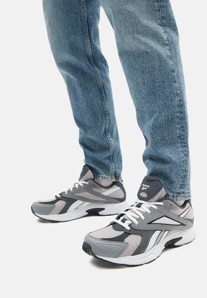 Zapatillas deportivas grises que combinan materiales de malla y sintéticos, con cordones y detalles blancos, sobre un fondo de jeans de mezclilla azules.