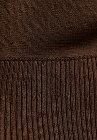 Primo piano di un tessuto a maglia marrone che mostra una superficie liscia nella parte superiore e una sezione inferiore a coste con dettagli di cucitura visibili.