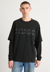 Juodas per didelis marškinėliai su apvalia iškirpte, su toniniu "HUGO" logotipu priekyje. Ilgos rankovės apačioje, medvilninė medžiaga, laisvas siluetas.
