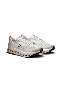 Lichte athletische schoenen in beige en wit met een ademend mesh bovenwerk, zwarte rubberen zool en een onderscheidende silhouet met uitsparingen.