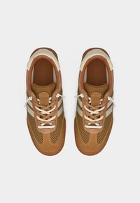 Ζευγάρι από καφέ και μπεζ αθλητικά παπούτσια με δίχτυ, με λευκά κορδόνια, τοποθετημένα δίπλα δίπλα σε λευκό φόντο.