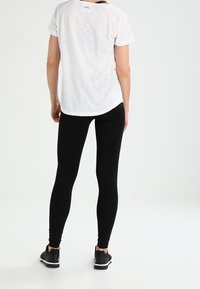 T-shirt blanc à manches courtes et col rond avec une légère texture, associé à des leggins noirs ajustés et des baskets noires. Design simple.