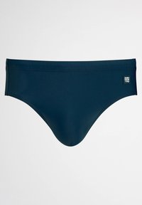 Námořnické modré plavky s hladkou texturou, jednoduchým designem a malou značkovou nášivkou na levé přední straně.