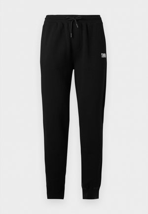 Črne ozke športne hlače z elastičnim pasom in vrvico za zategovanje, zankami na gležnjih ter majhnim belim napisom "KARL LAGERFELD" na desnem boku.