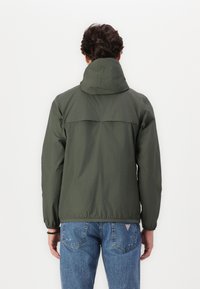 Chaqueta ligera de color verde oscuro con capucha, puños y dobladillo elásticos. Presenta un diseño de yugo en la parte superior de la espalda y una textura suave.