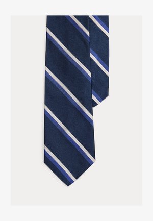 Cravată bleumarin cu dungi diagonale albe și nuanțe diferite de albastru pe un fundal simplu deschis.