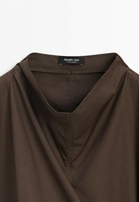 Ciemnobrązowy kołnierz koszuli z dekoltem w kształcie litery V oraz czarną metką Massimo Dutti przyszytą od wewnątrz.