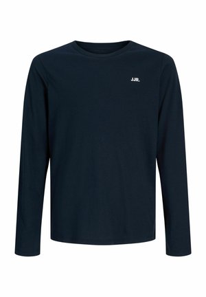 Garçon blond debout portant un t-shirt à manches longues bleu marine avec le texte « JJR. », un pantalon vert olive et des chaussures marron à lacets sur fond blanc.