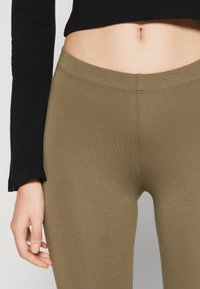 Khaki leggings made from stretchy fabric with a smooth texture and a seamless waistband, paired with a black long-sleeve top.