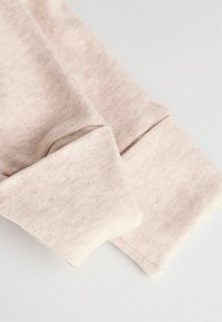Tessuto rosa chiaro con una superficie morbida e testurizzata. Presenta polsini arrotolati e un sottile motivo melangiato. Cuciture piatte visibili ai bordi.