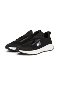 Fekete kötött sportcipők, fehér talppal, lapos fűzőkkel és piros, fehér és kék Tommy Jeans logóval az oldalon.