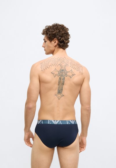 Cuecas masculinas em azul marinho com cintura elástica de marca. Textura de tecido suave, design minimalista e ajuste justo. Vista traseira mostra detalhes de tatuagens.