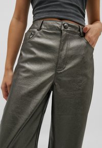 Pantalons larges en simili cuir gris métallique avec une taille haute, des poches avant et des coutures visibles. Texture lisse avec un léger éclat.