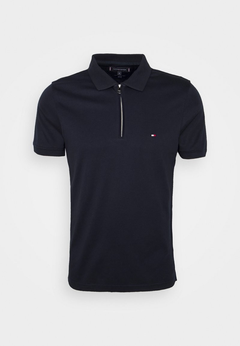 Polo bleu marine à manches courtes avec col, fermeture éclair argentée à l'avant et petit logo rouge, blanc et bleu sur la poitrine.