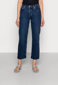 Tmavě modré, vysokým pasem, široké džíny s jemným vybledlým vzorem, s páskovými smyčkami a knoflíkovým zapínáním. V kombinaci se světle modrými sandály.