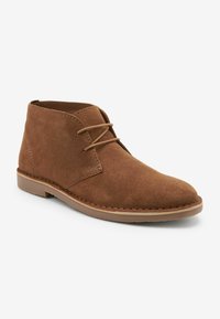 Botas desierto de ante marrón con punta redonda, dos ojales y una suela de goma ligera marrón cosida. Textura suave con un detalle mínimo.