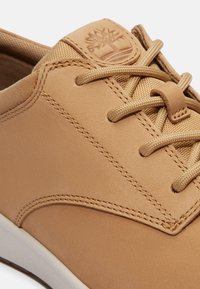 Zapatillas de cuero marrón con un acabado suave, cordones redondos, acentos con costuras y un logo en relieve en la lengüeta. Suela de goma blanca.