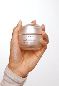 Shiseido Benefiance Wrinkle Smoothing Cream in a round glass jar with a metallic silver lid, held in a hand. Smooth, transparent texture.