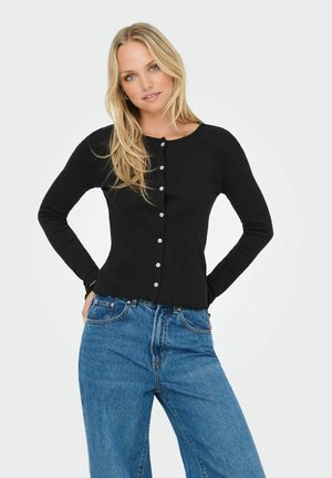 Sort ribbet langærmet cardigan med knapper foran og flæset kant. Kombination med lyseblå vide ben jeans.