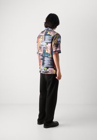 Short-sleeve shirt made of lightweight fabric featuring a colorful, abstract pattern with various shapes and text; paired with black trousers.