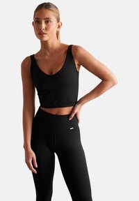 Zwarte geribbelde crop top met brede banden, gecombineerd met high-waisted zwarte geribbelde leggings. Glad, rekbaar materiaal met minimale logo-detail.