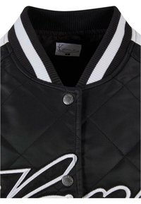 Black quilted jacket with a ribbed collar, featuring white striped accents, snap button closure, and large white embroidered detail.